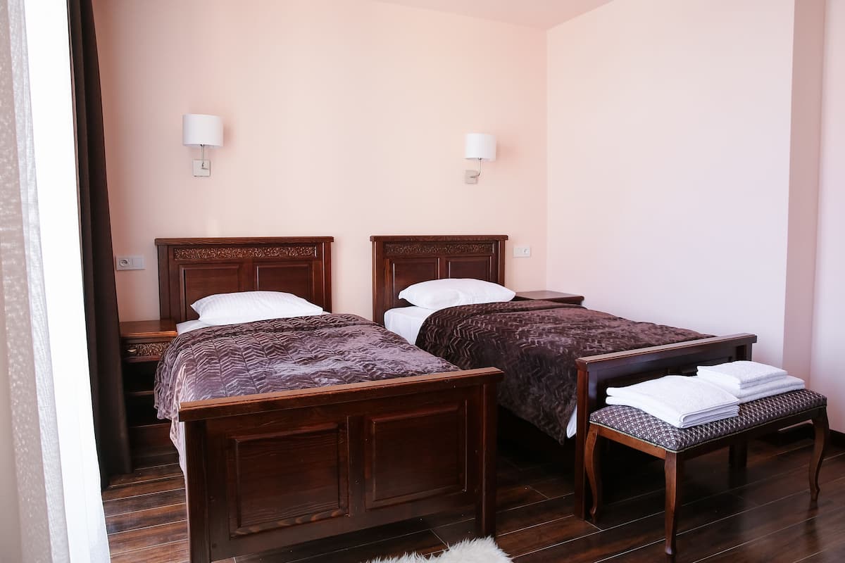 A hotel room with two wooden beds, a bench with towels, and two bedside lamps.