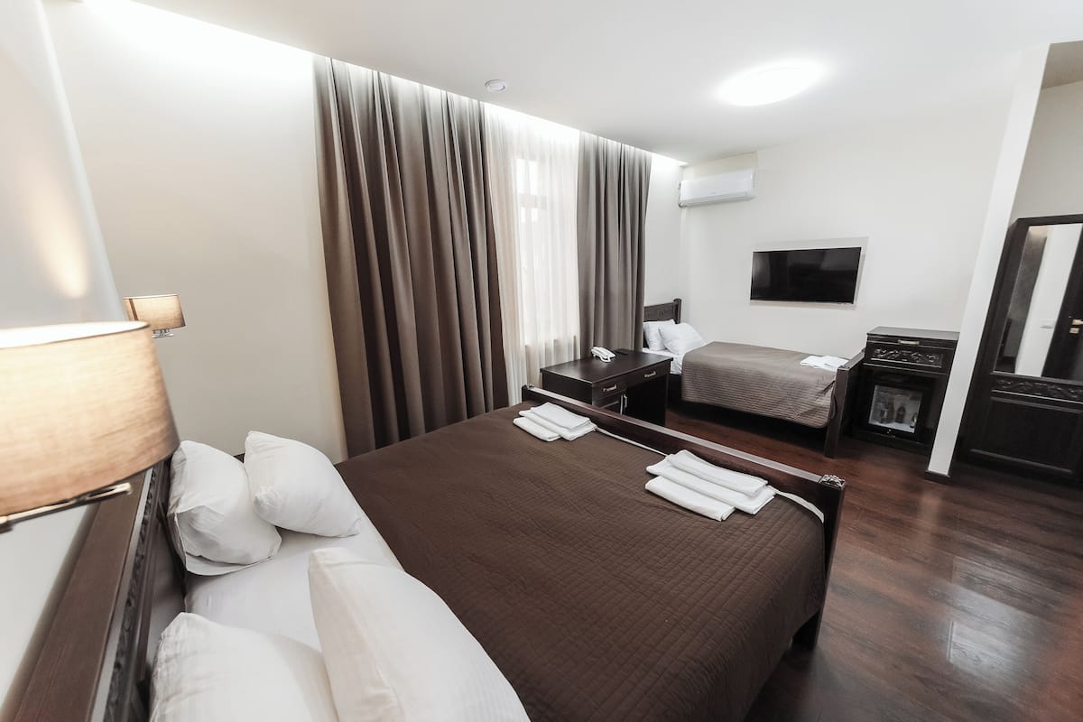 A hotel room with a large bed, a smaller bed, a desk with a TV, and a mirror.