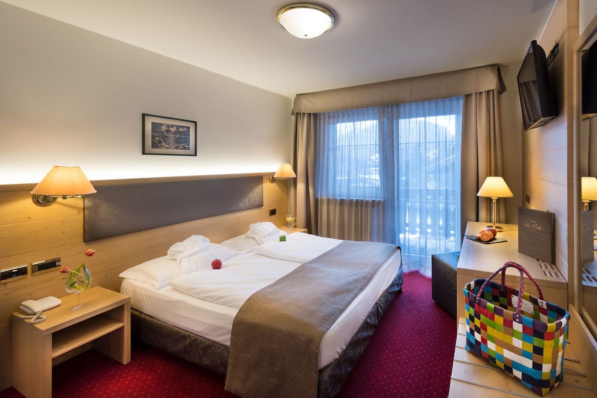 A hotel room with a bed, bedside tables, a desk, a chair, a TV, and a window with curtains.