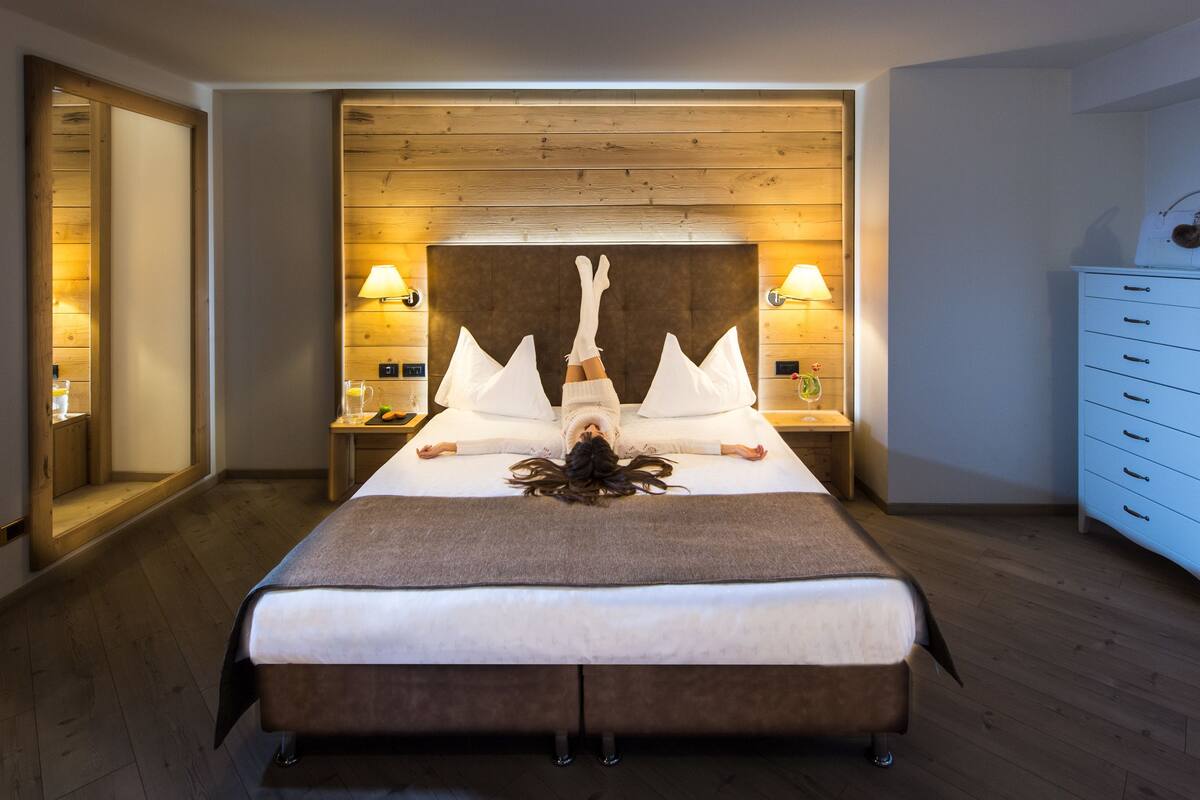 A hotel room with a large bed, wooden headboard, bedside lamps, a dresser, and a mirror.