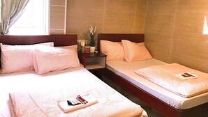 Ein Hotelzimmer mit zwei Betten, jeweils mit einer rosa geblümten Tagesdecke und passenden Kissen. Ein kleiner Tisch mit einer Pflanze und einem roten Gegenstand, möglicherweise einer Flasche, steht ebenfalls im Raum.