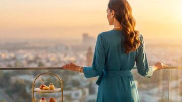 Una persona está de pie en un balcón con vistas a una ciudad, con un soporte escalonado para postres y una taza sobre una mesa.