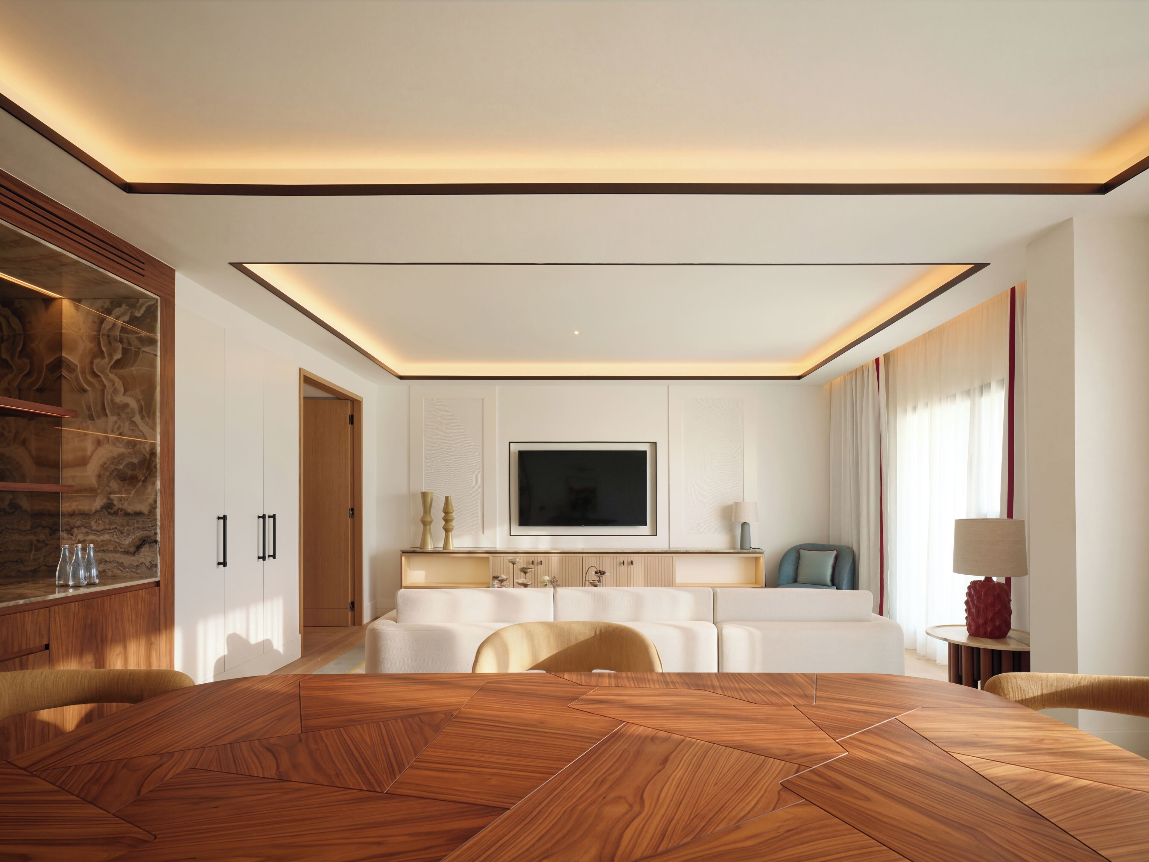 Une chambre d’hôtel moderne avec une table à manger en bois, un canapé et un téléviseur fixé au mur.