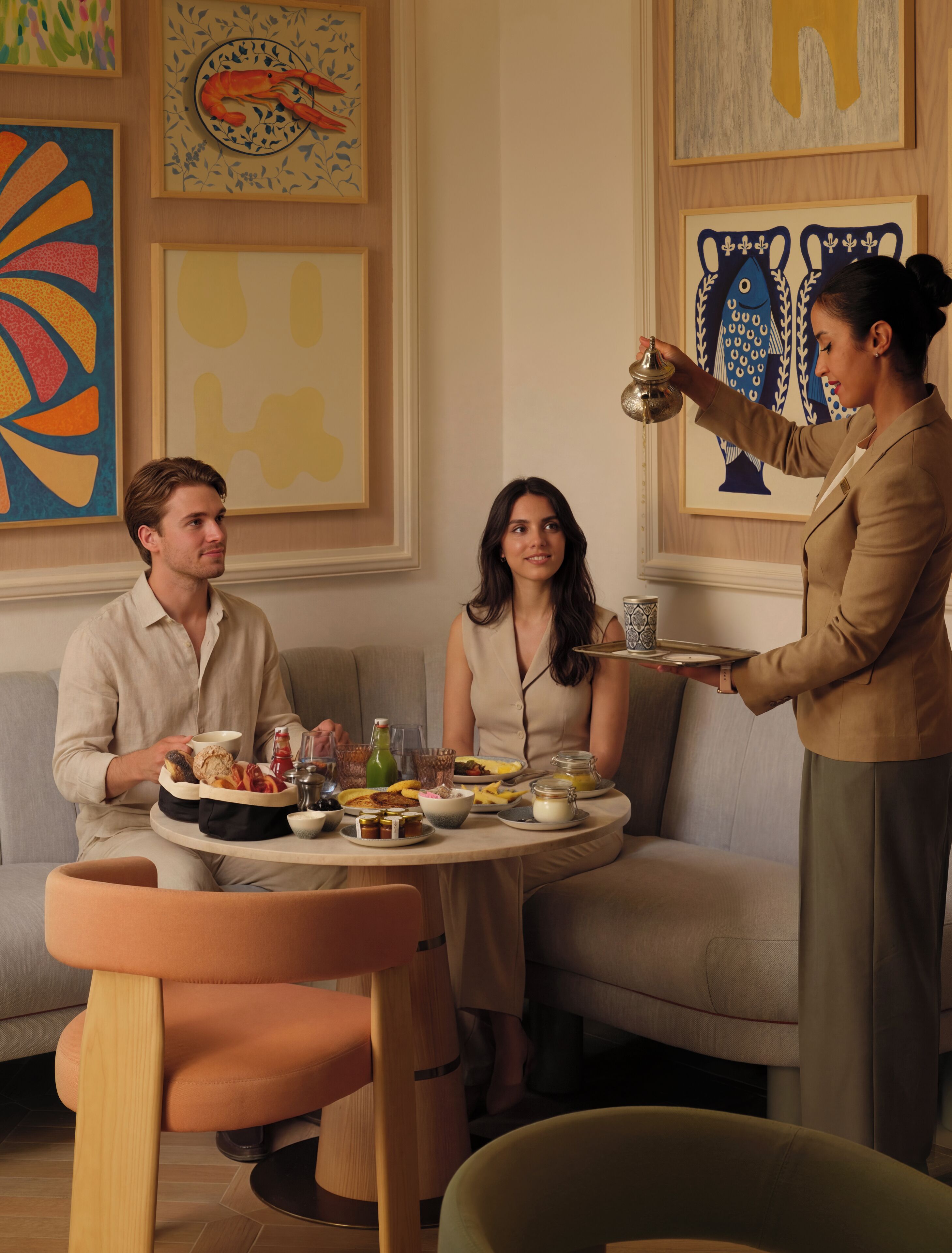 Un coin repas avec une table ronde dressée pour trois personnes, entouré d’œuvres d’art moderne et d’un canapé.