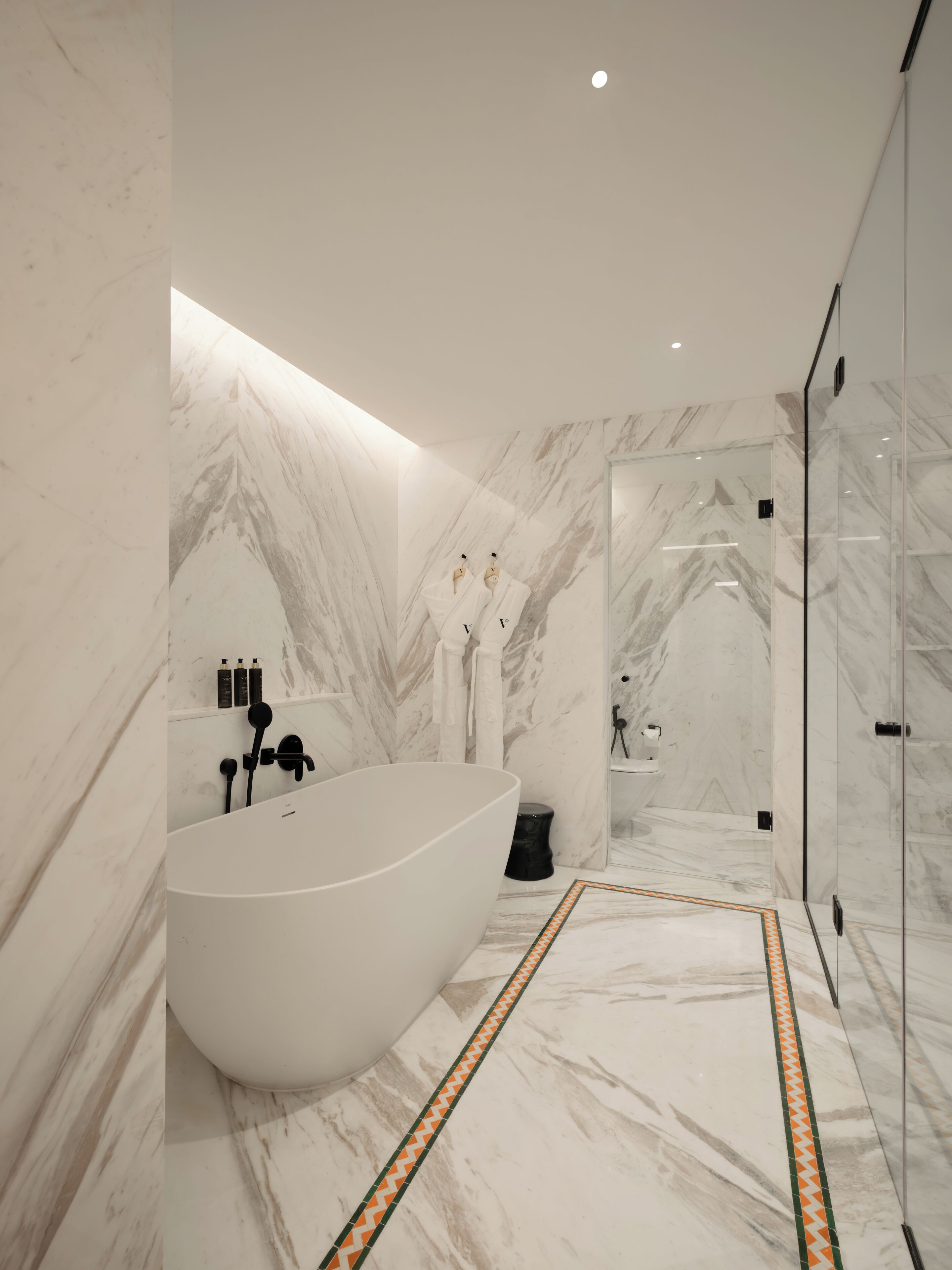 Un baño moderno con una bañera independiente, paredes de mármol y un box de ducha de vidrio.