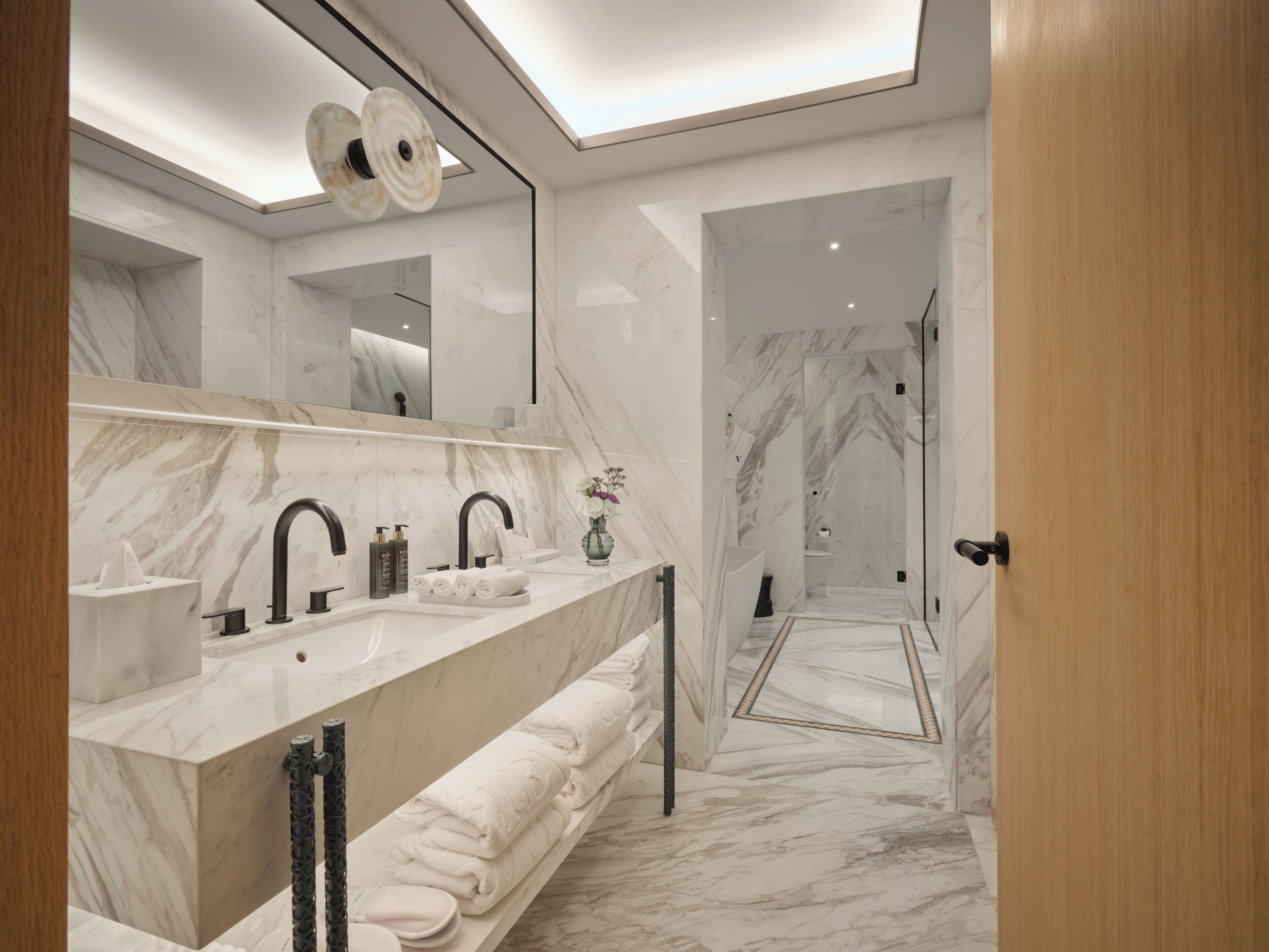Un baño moderno con encimera de mármol, grifos negros y un espejo grande.