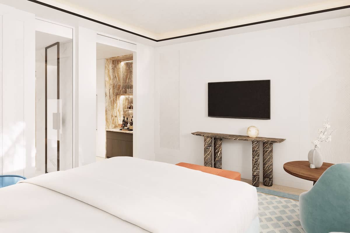 Una habitación de hotel con una cama, una mesita con un florero, una silla y un televisor en la pared.