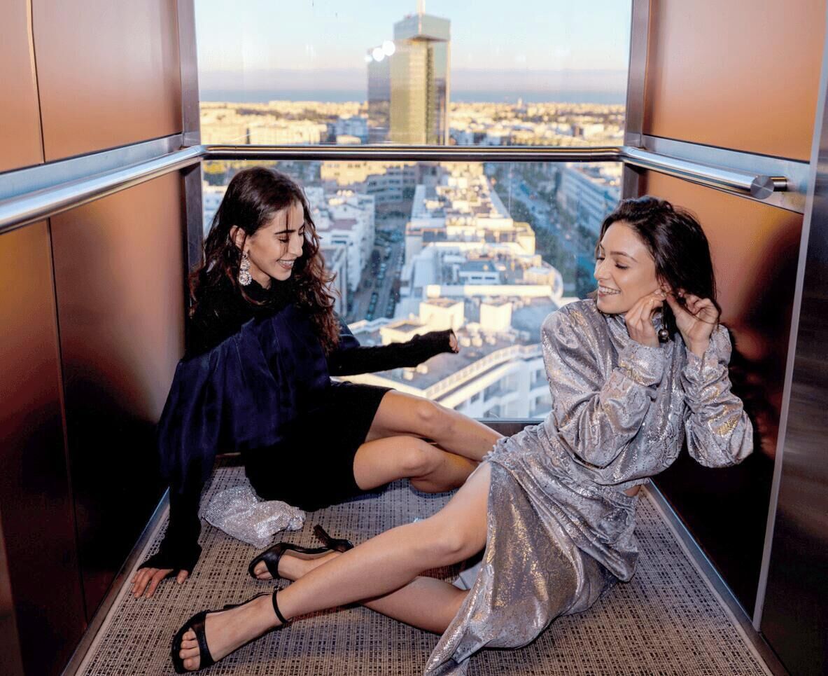 Two individuals seated in a high-rise interior with a cityscape view.