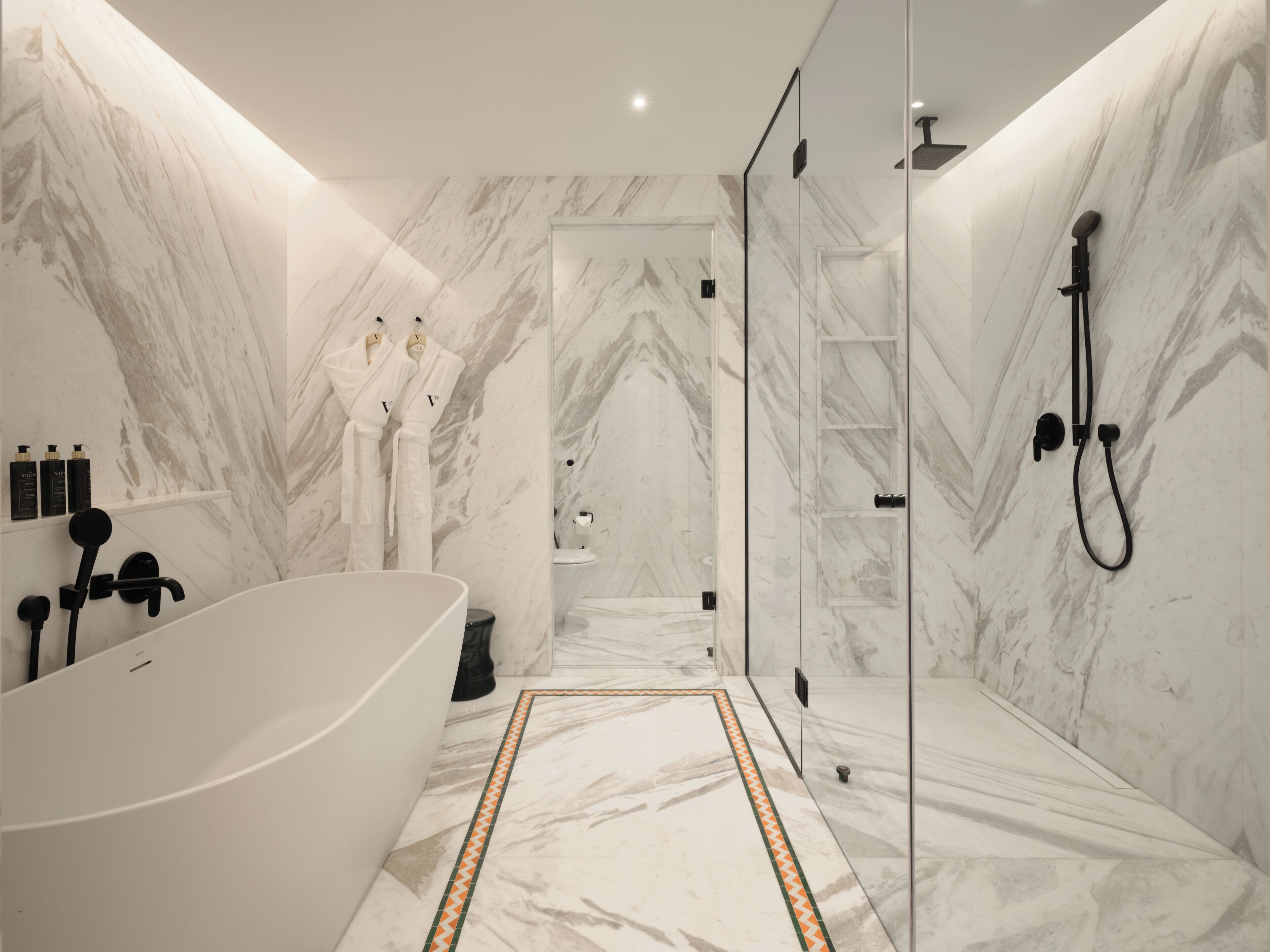 A modern bathroom with a freestanding bathtub, a glass-enclosed shower, and marble walls.