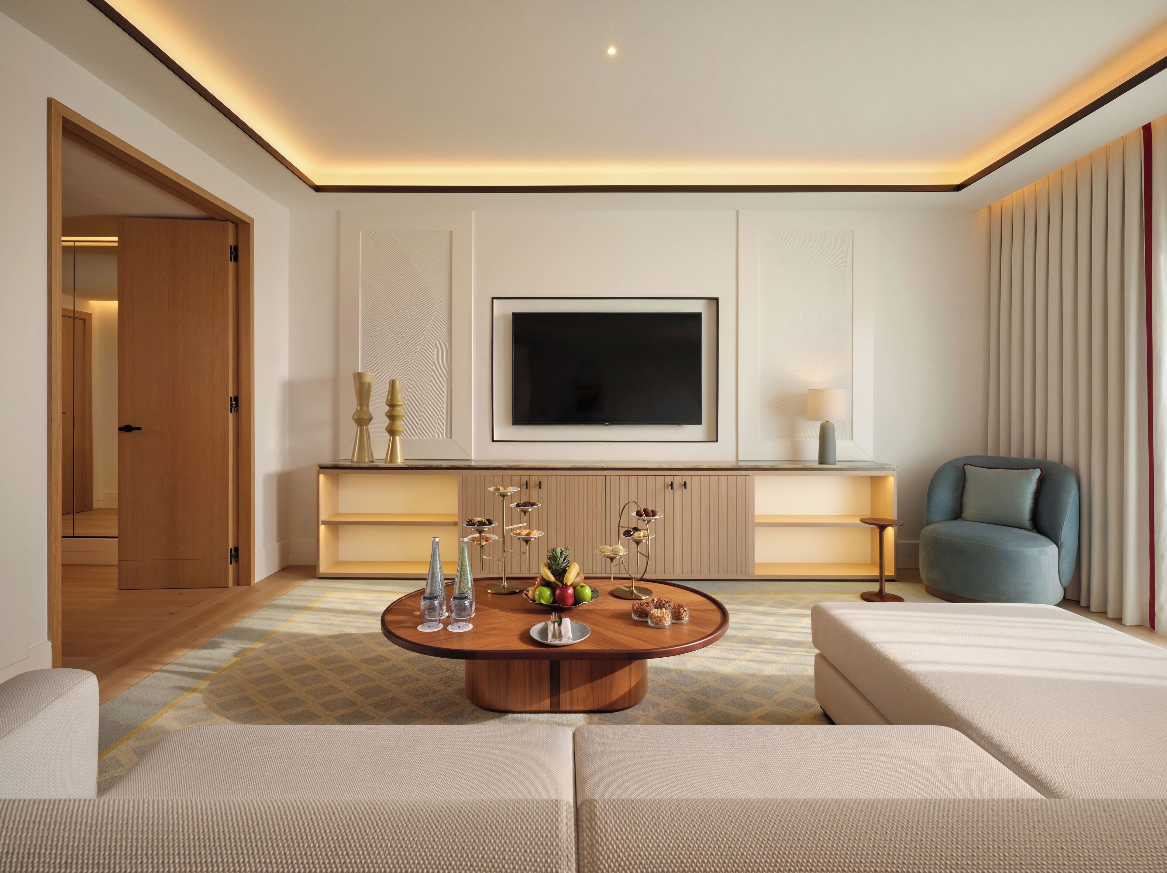Ein modernes Wohnzimmer mit einem Holztisch, einem flachbildfernseher an der Wand und einer Sitzecke mit blauem Sessel.