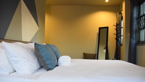 Una cama bien hecha con almohadas blancas y azules, una toalla blanca enrollada y un espejo grande en la pared.
