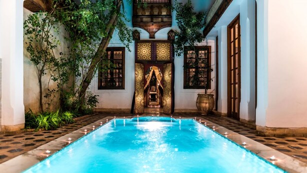 Una piscina con un diseño geométrico de azulejos, rodeada de muros con detalles de madera decorativa y plantas.