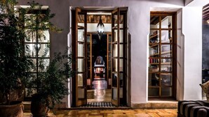 Un pasillo con piso de madera y puertas abiertas que dan a una biblioteca y un salón con sofá.