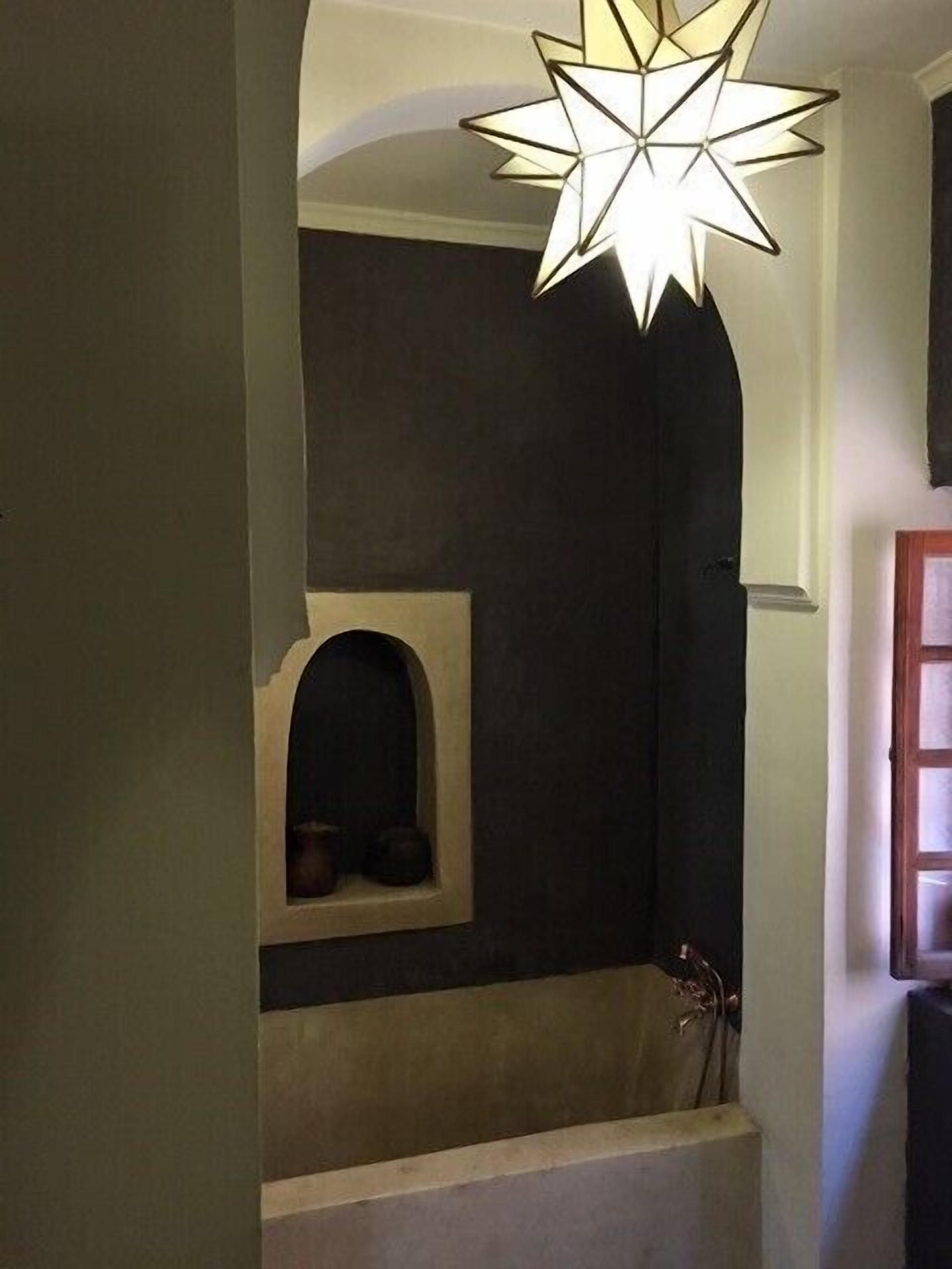 A staircase with a star-shaped light fixture above, leading to a dark wall with a small alcove containing two pots.