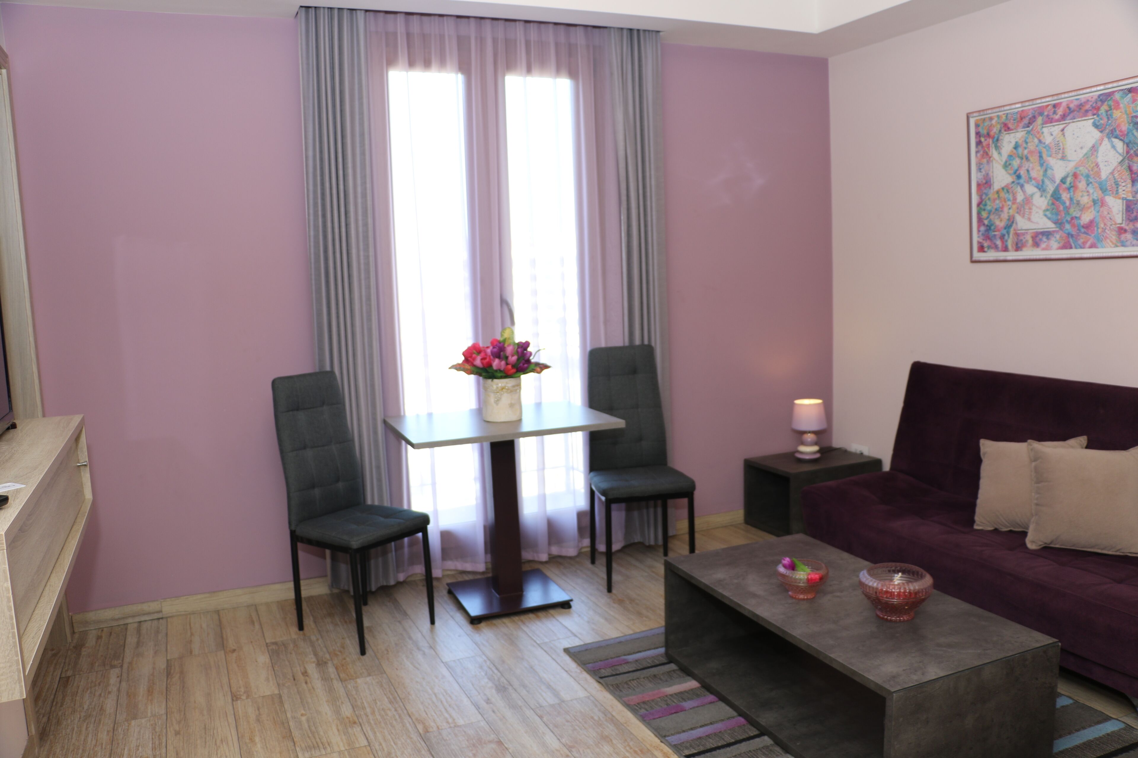 Una sala de estar moderna con una pared morada, una mesa de vidrio con dos sillas, un sofá y una mesa de centro con objetos decorativos.