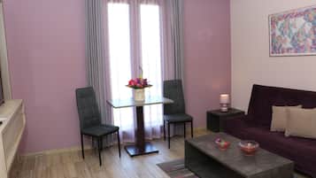 Una sala de estar moderna con una pared morada, una mesa de vidrio con dos sillas, un sofá y una mesa de centro con objetos decorativos.