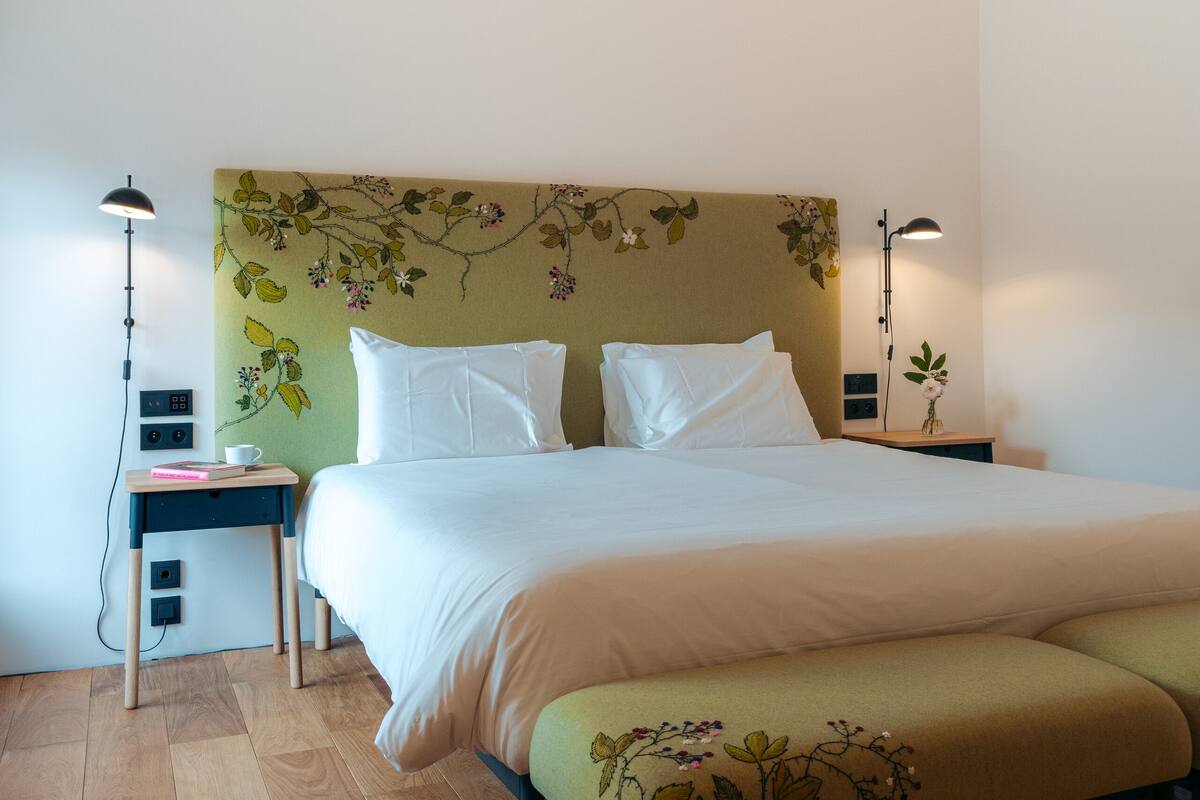 A neatly arranged bedroom with a large bed, bedside tables, a bench, and a floral headboard.
