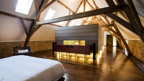 A bedroom with a wooden ceiling, a bed, a dresser, and a brick wall. - Indrani Lodge (Genappe)