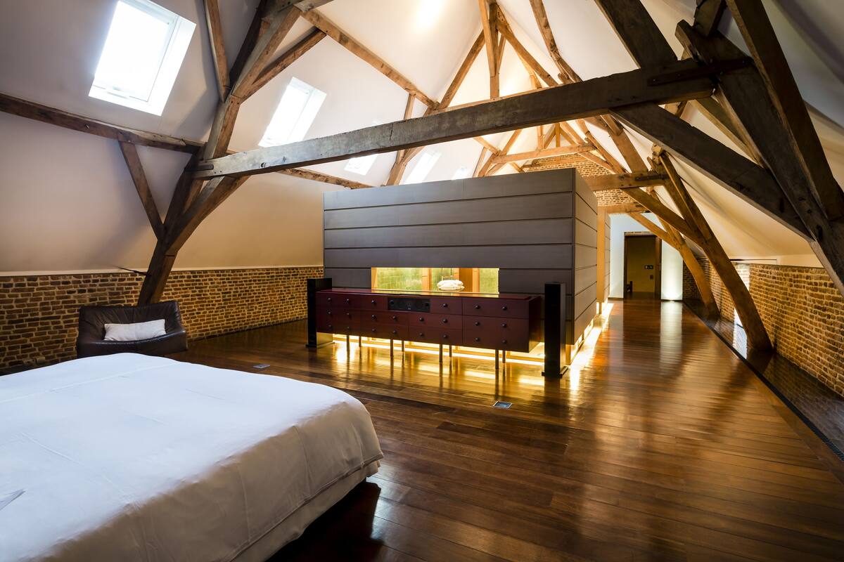 A bedroom with a large bed, wooden beams, a brick wall, and a dresser with drawers.