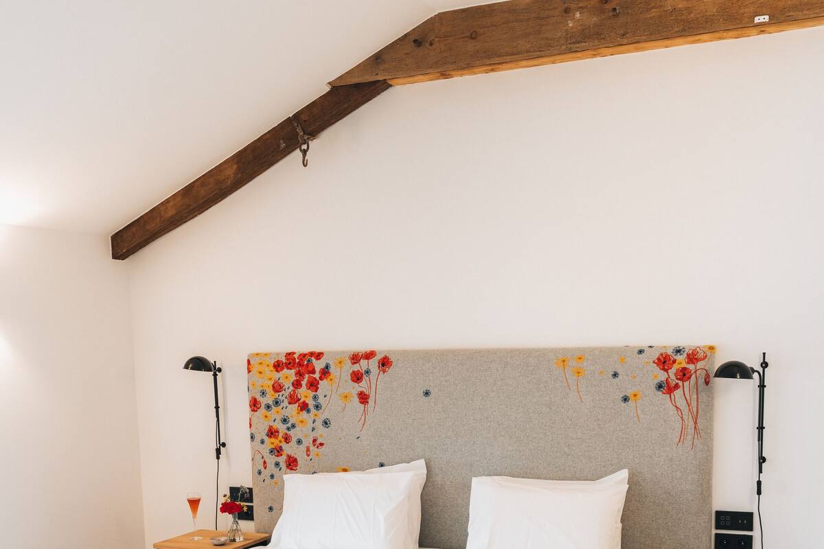 A bedroom with a wooden ceiling, a bed with white bedding, two bedside tables, and a bench at the foot of the bed.