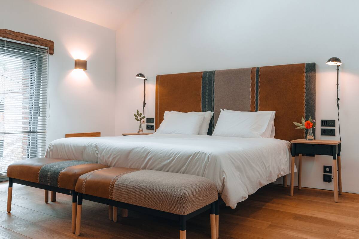 A neatly made bed with white linens, a wooden headboard, and two bedside lamps.