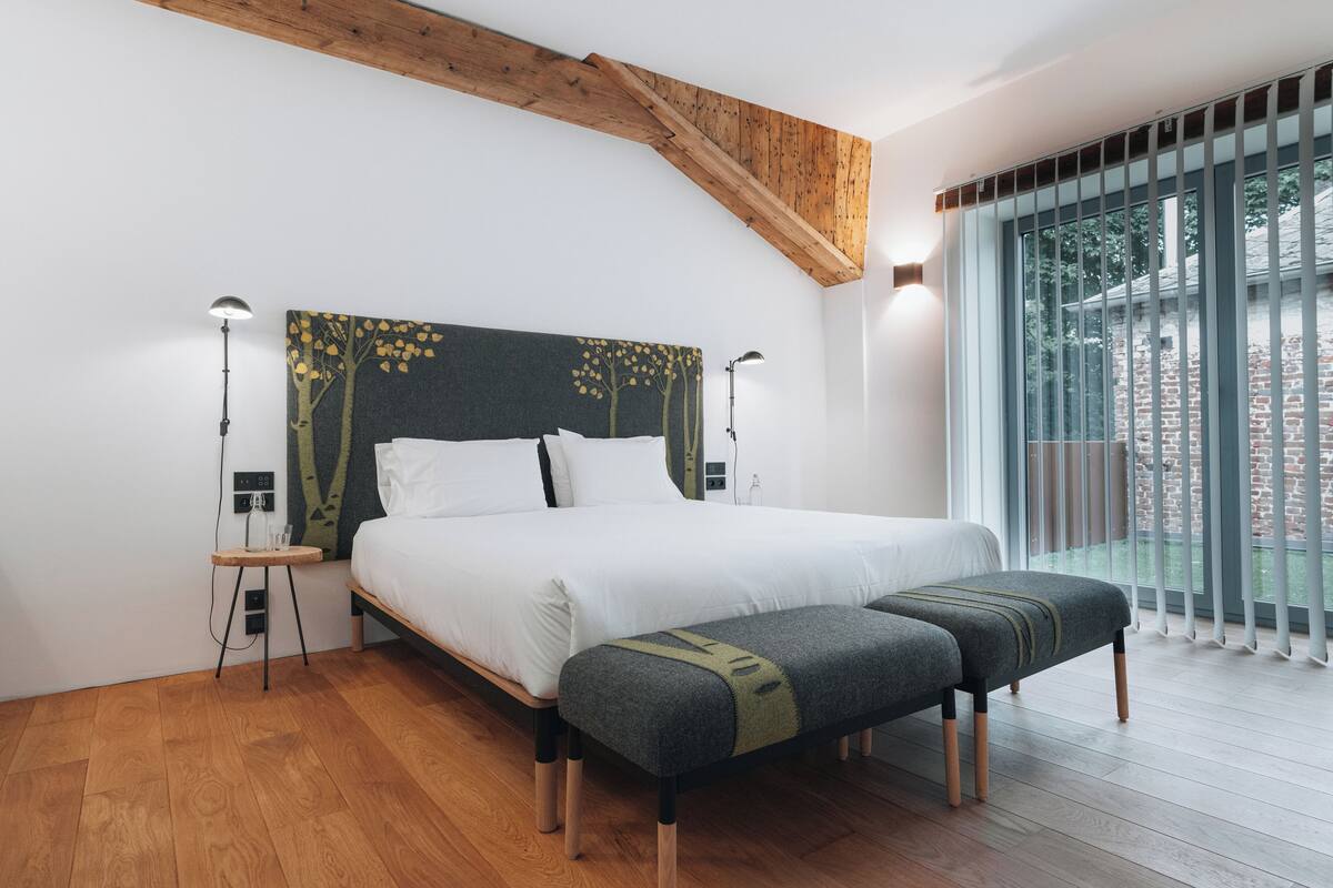 A modern bedroom with a large bed, a bench, and a view of the outside.
