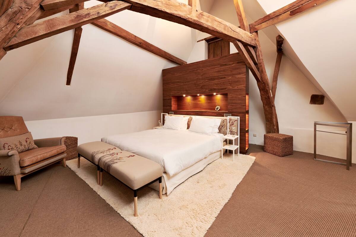 A bedroom with a large bed, a wooden headboard, a nightstand, a bench, and a small table.
