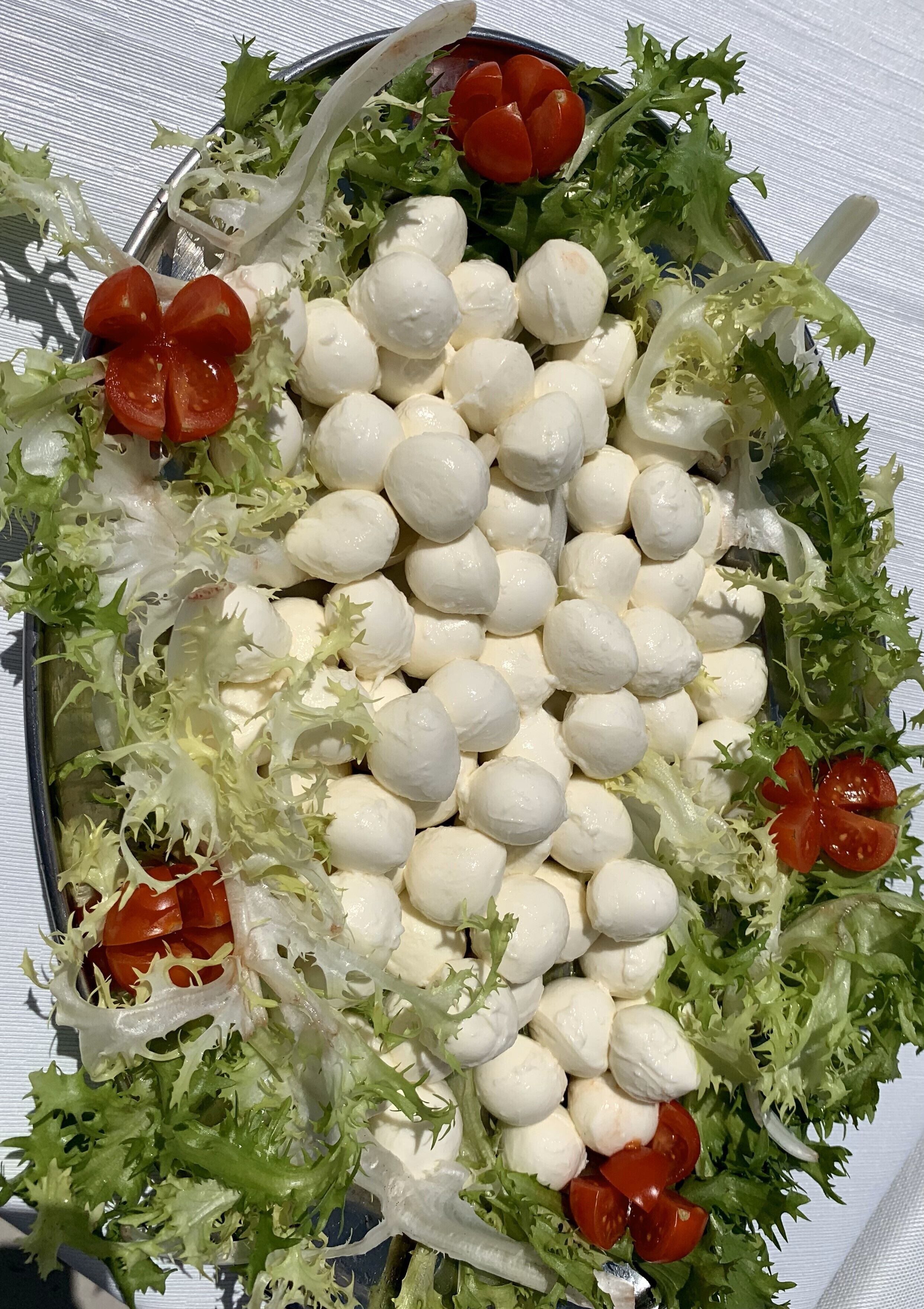 A tray of mozzarella balls and cherry tomatoes on a bed of mixed greens.