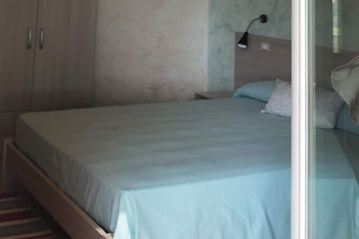A bedroom with a bed, a nightstand, a lamp, and a wardrobe.