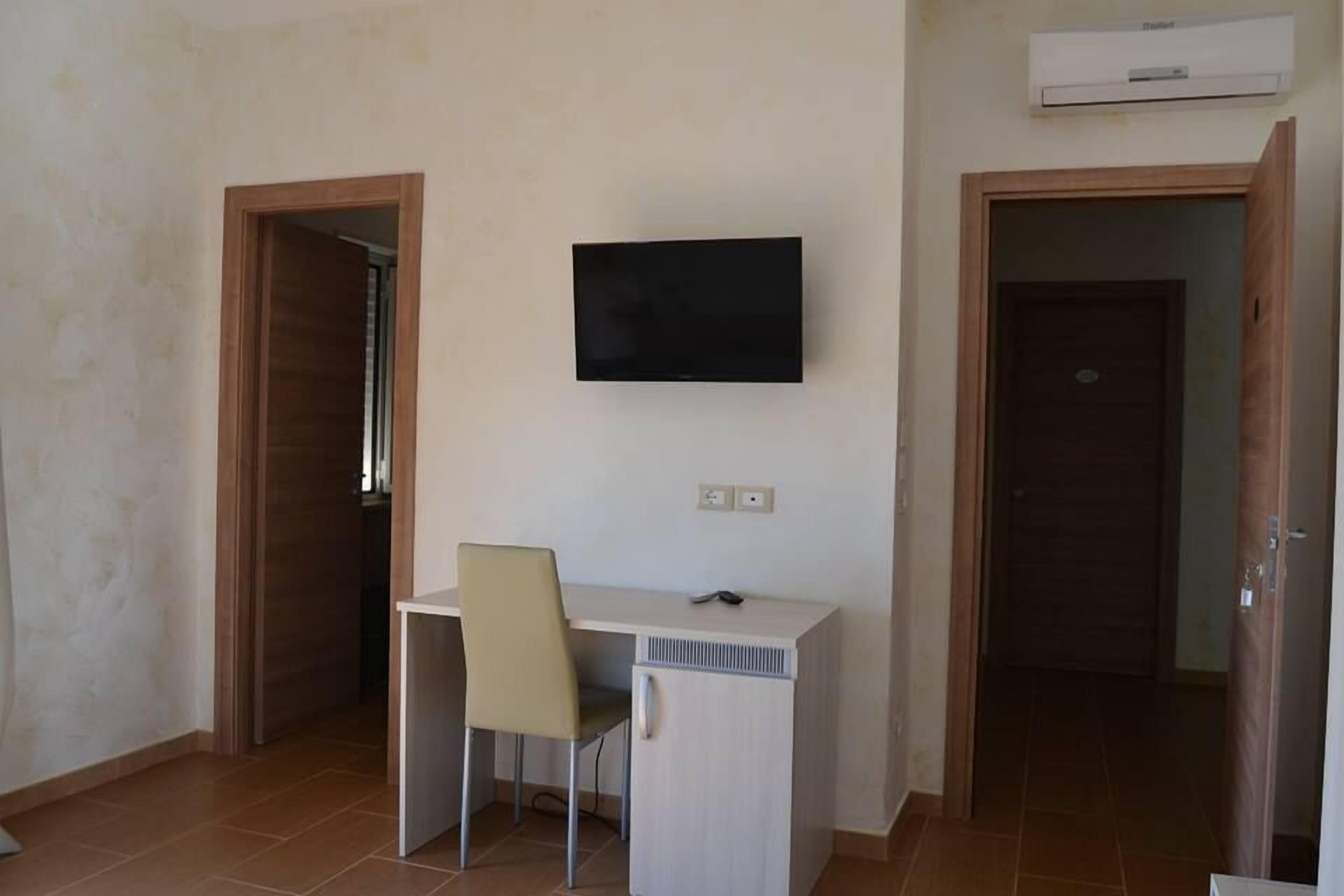 Quarto com escrivaninha, cadeira, televisão e ar condicionado.