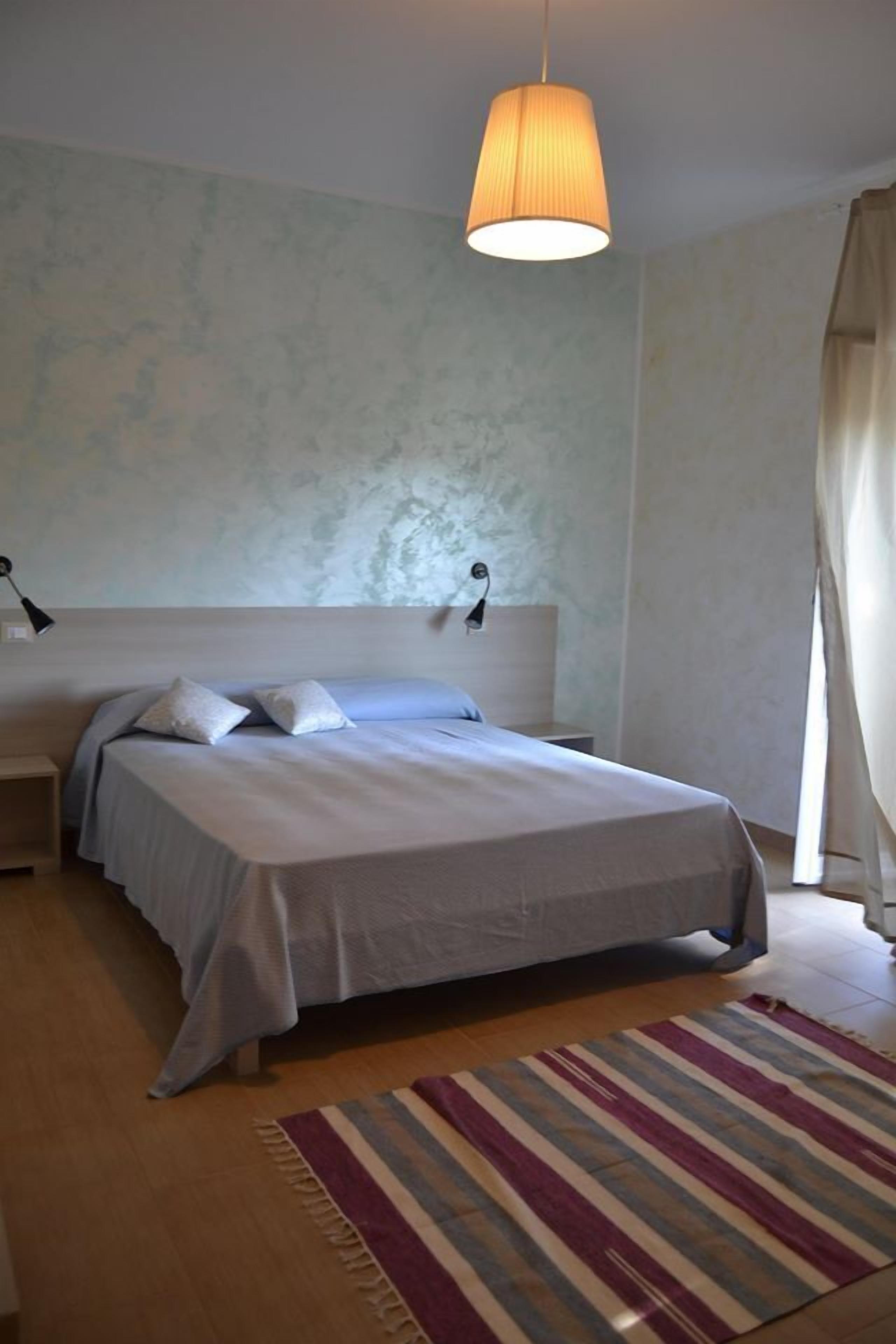 Ein Schlafzimmer mit einem Bett, Nachttischen, einer Hängelampe und einem Streifen Teppich.