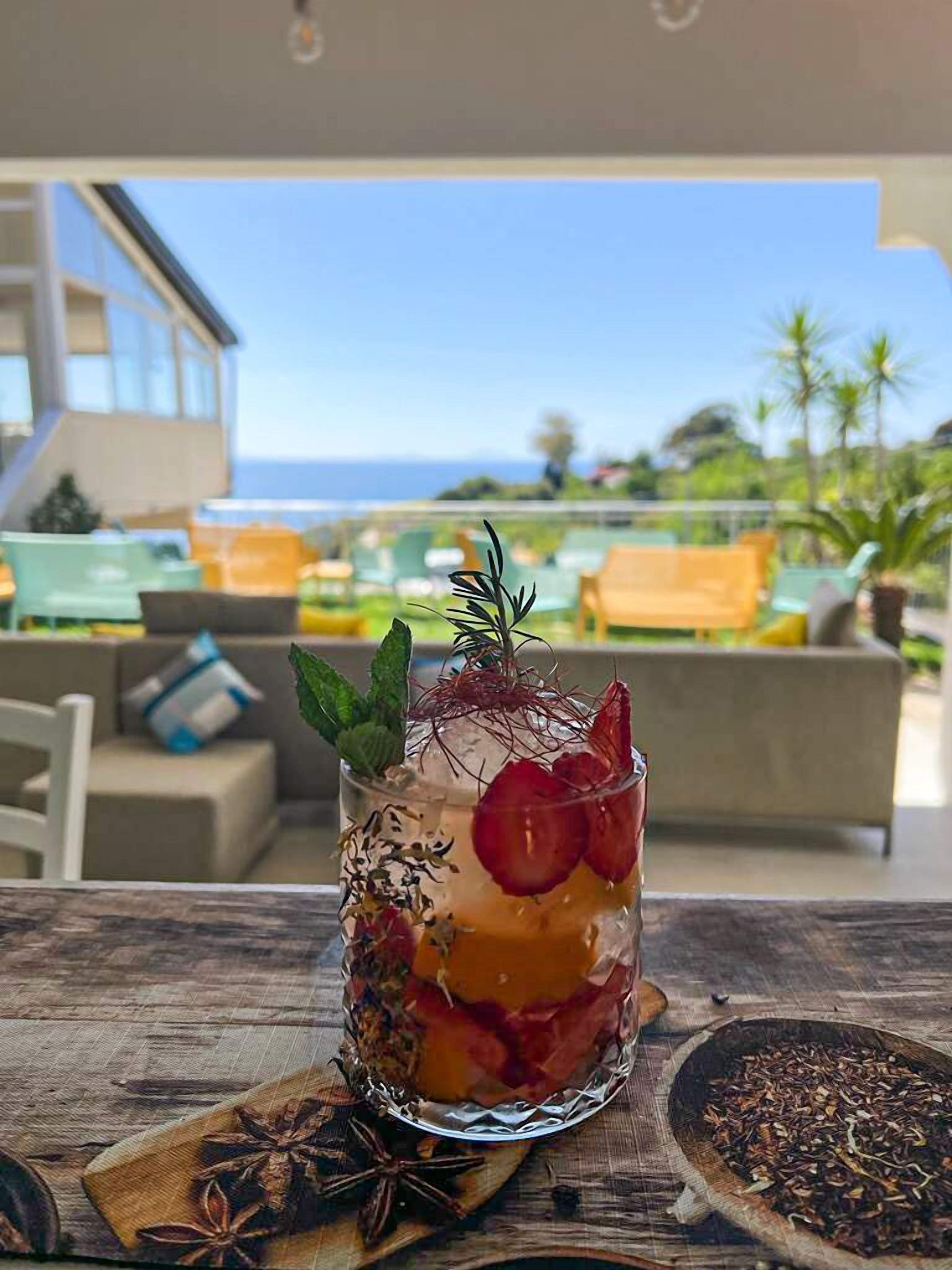 A cocktail glass with a garnish on a wooden table, with a view of a modern building and a balcony in the background.