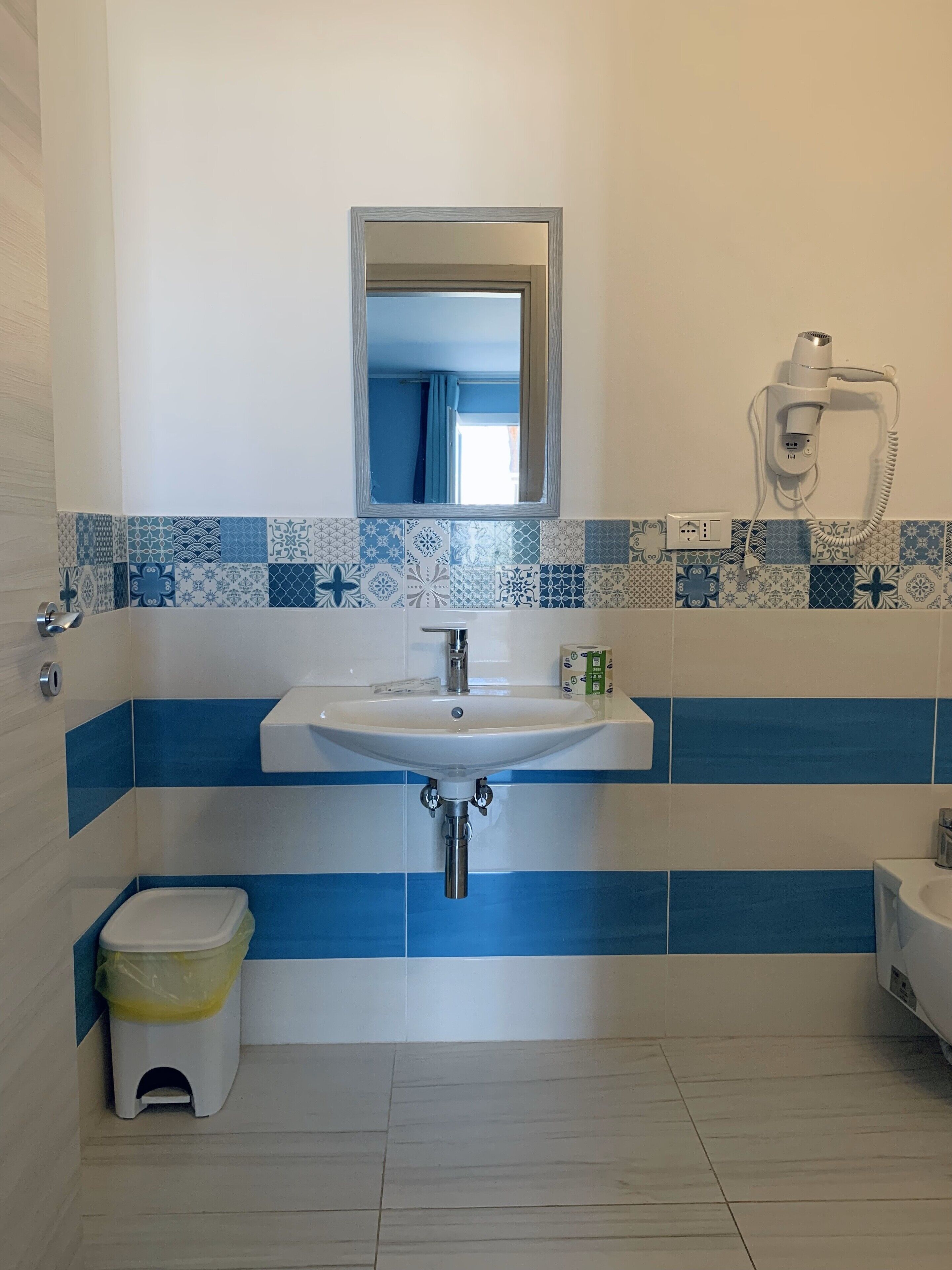 A bathroom with a white sink, a mirror above it, and a hairdryer on the wall.