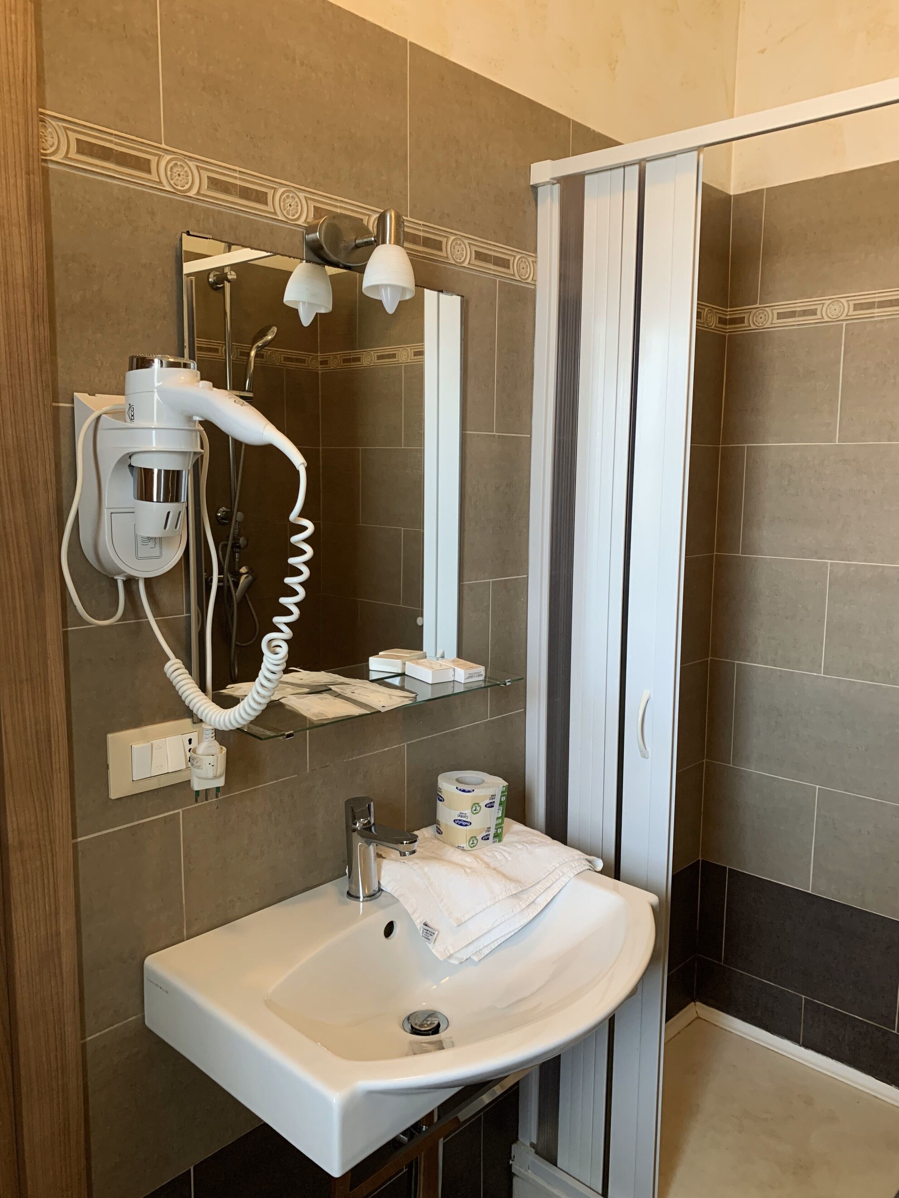 A bathroom with a white sink, a hairdryer, a mirror, and a shower area.