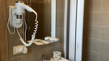 A bathroom with a white sink, a hairdryer, a mirror, and a shower area.