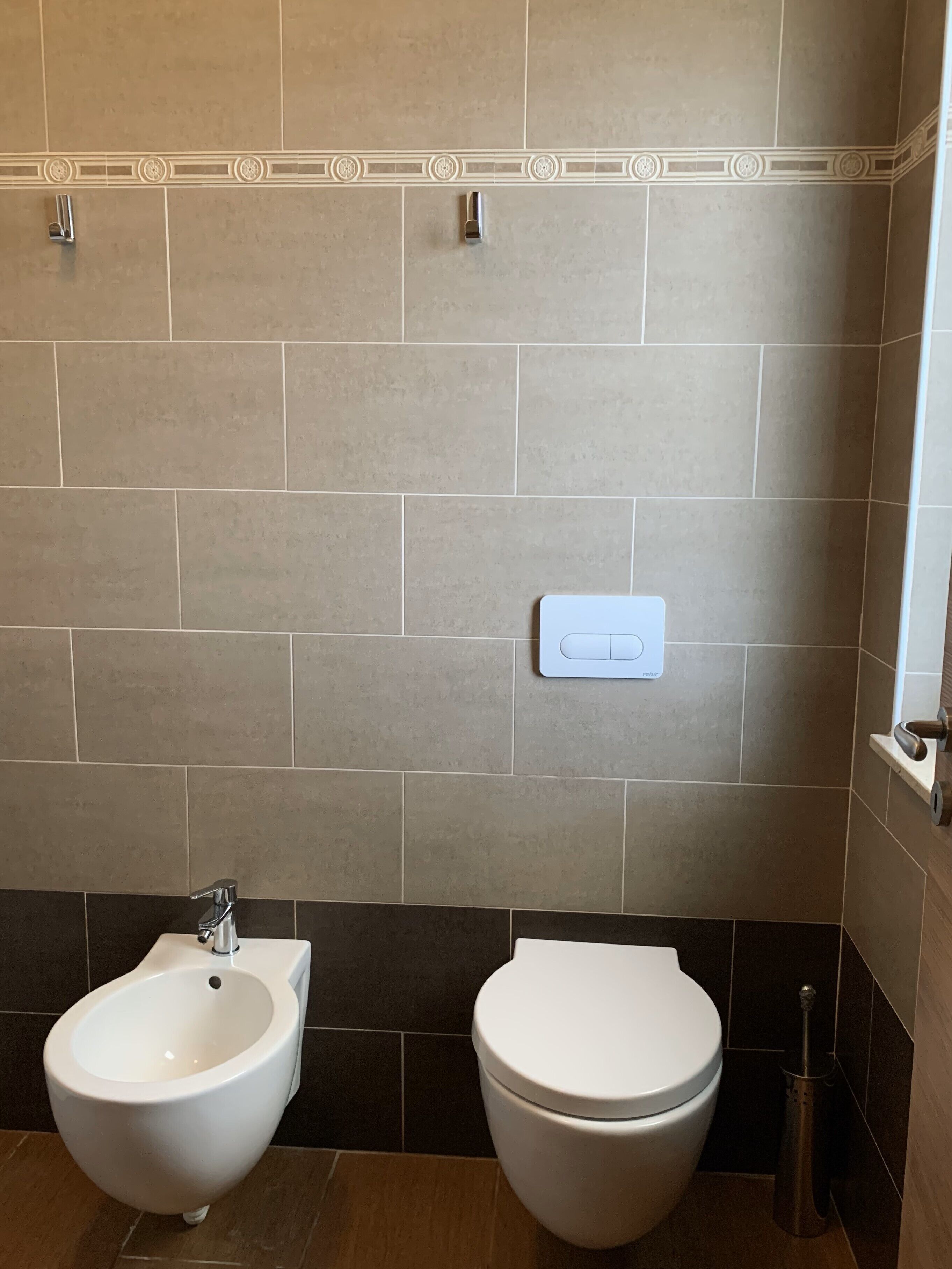 Een badkamer met een toilet, een bidet en een lichtschakelaar op de muur.