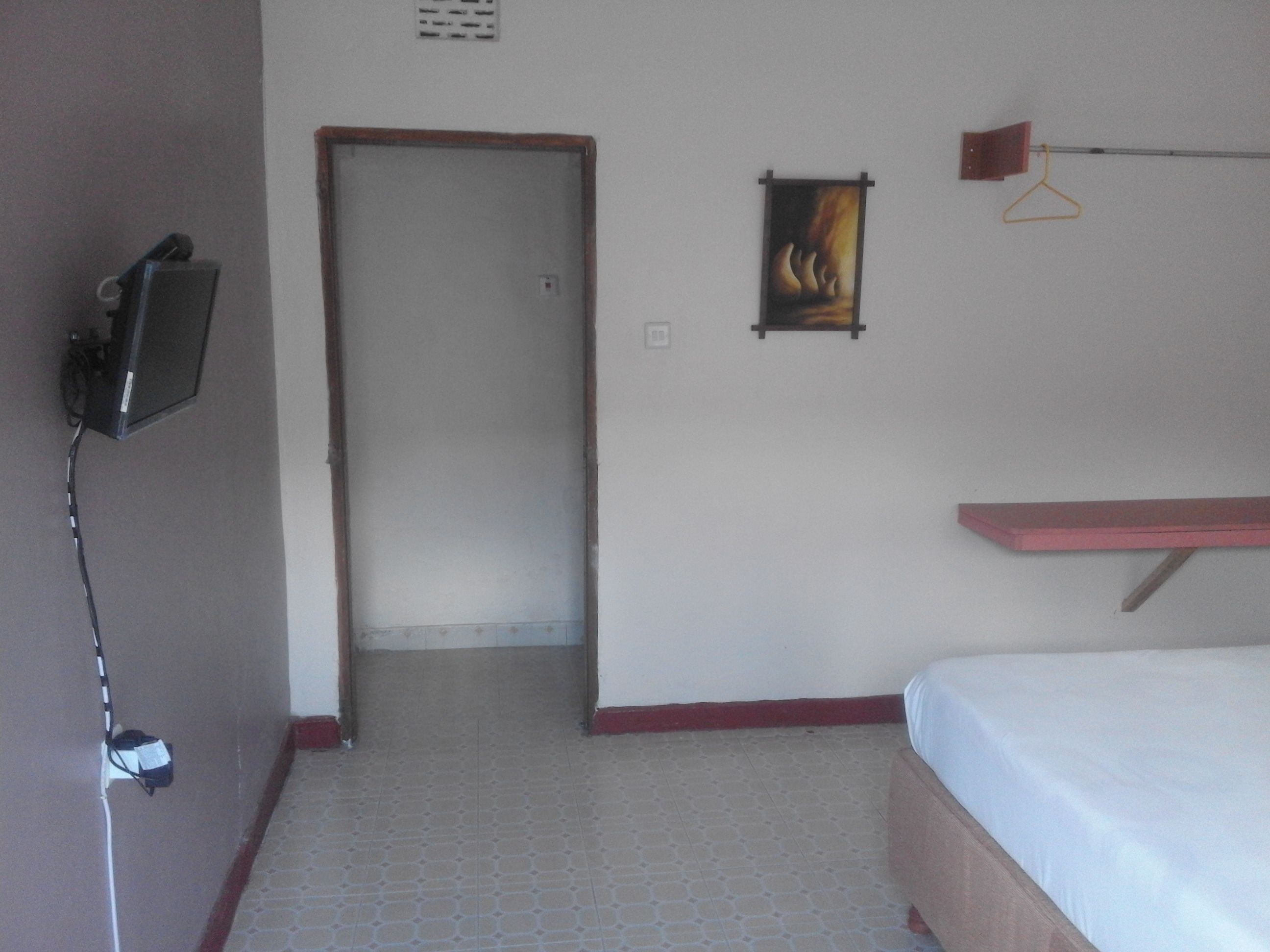 Una habitación de hotel con una cama, un televisor en la pared, una puerta y un pequeño cuadro.