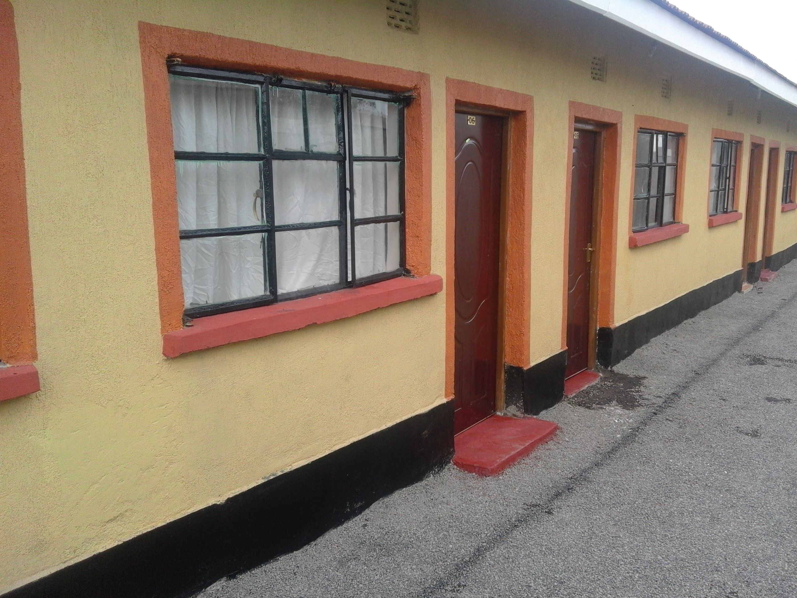Una hilera de habitaciones con marcos rojos en ventanas y puertas, un muro exterior amarillo y un zócalo negro.