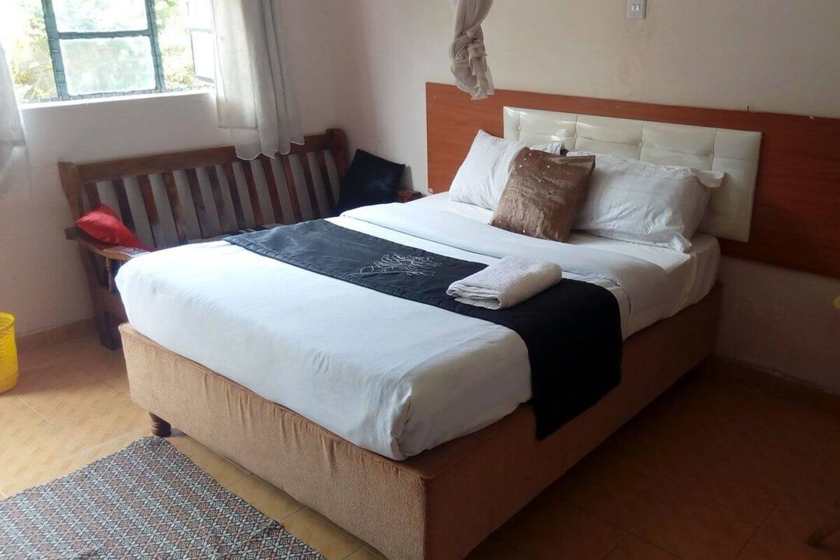 Una cama bien hecha con cabecera de madera, una mesita de noche y una silla.
