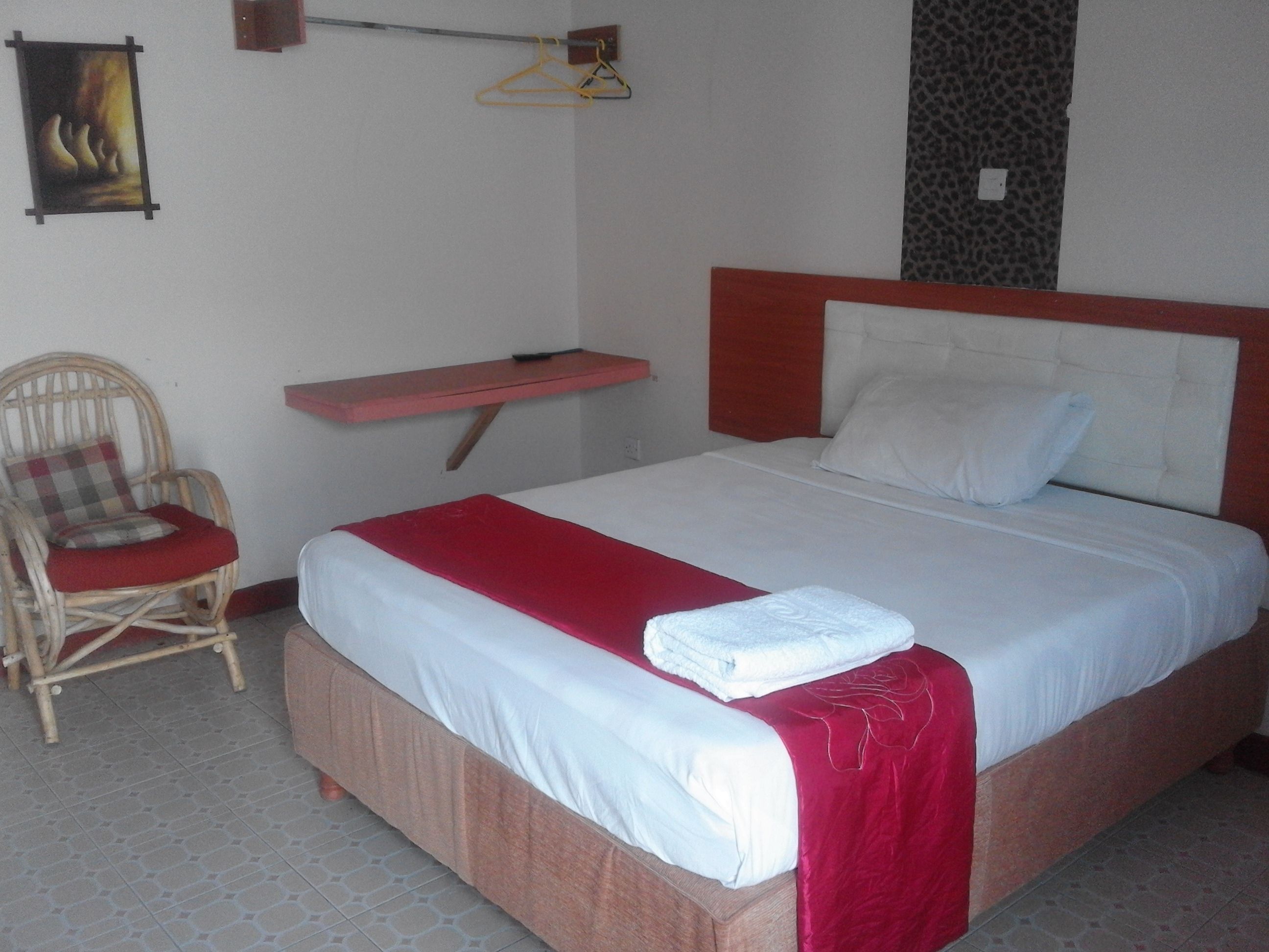 Habitación de hotel con cama, una silla, una mesita y estante en la pared.