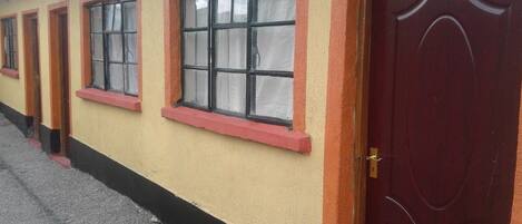Un hilera de habitaciones con ventanas de marco rojo y una puerta rojo oscuro con el número '06'.
