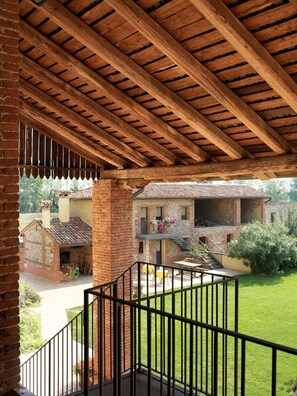 A covered outdoor area with a wooden ceiling and brick walls, leading to a courtyard with a grassy lawn and a building with a tiled roof. - Agriturismo Borgo Tecla (Rosa)