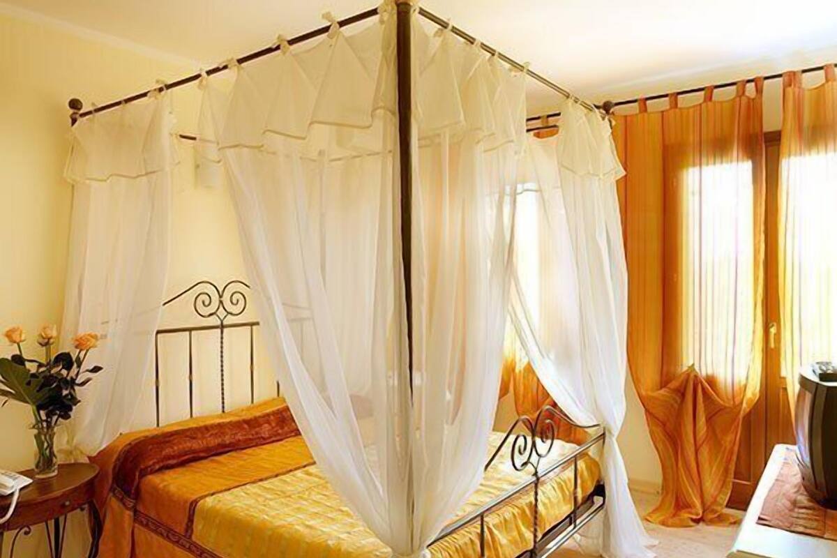 A four-poster bed with a canopy, a bedside table with a vase of flowers, and a window with curtains.