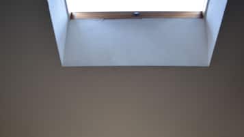 A bedroom with a skylight, a bed with white linens, two bedside tables, and two wall-mounted lights.