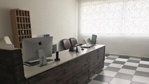 Un comptoir d’accueil avec un ordinateur, deux chaises, une bibliothèque et une fenêtre décorée.