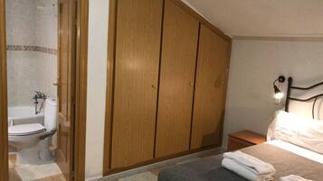 Un dormitorio con cama, mesita de noche, armario de madera y baño con inodoro y ducha.