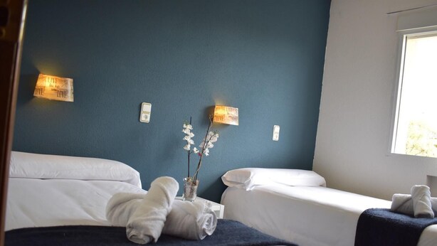 Une chambre d’hôtel avec deux lits, un vase de fleurs et des lampes fixées au mur.