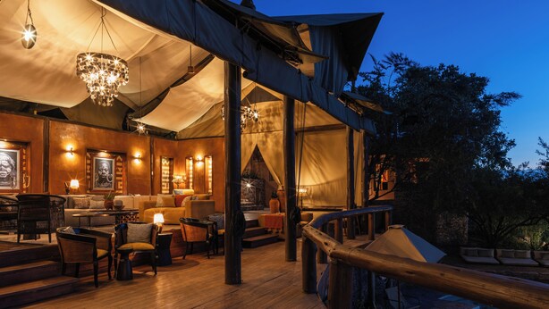A tented outdoor area with wooden flooring, seating arrangements, and a staircase leading to a higher level. - Elewana Serengeti Migration Camp (Serengeti)