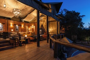 A tented outdoor area with wooden flooring, seating arrangements, and a staircase leading to a higher level. - Elewana Serengeti Migration Camp (Serengeti)