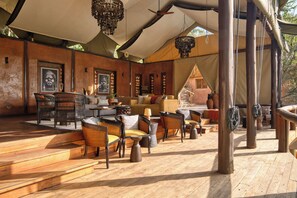 An outdoor seating area with wicker furniture, a wooden floor, and a tent structure. - Elewana Serengeti Migration Camp (Serengeti)